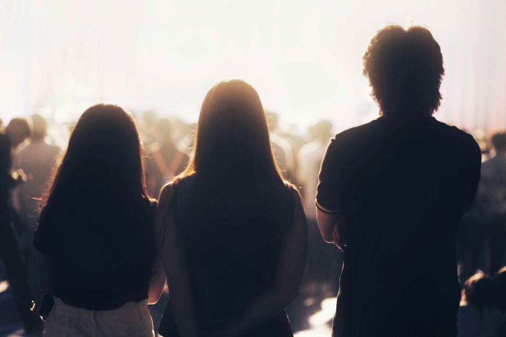Three teens watching a crowd from the sidelines.